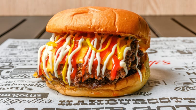 A double cheeseburger with melted cheese, ketchup, mustard, and mayonnaise on a branded paper.