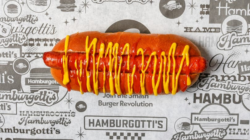 A Hamburgotti's hot dog with ketchup and mustard on branded paper from above.