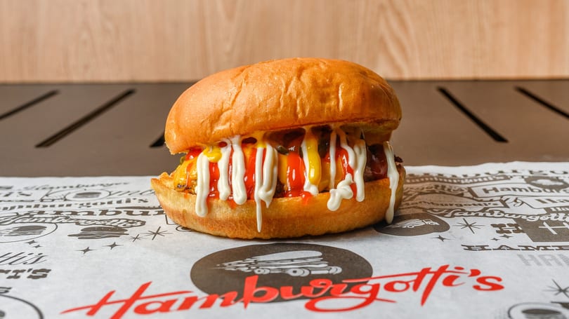 A HamburGotti's burger with ketchup, mustard, and mayonnaise on branded paper.