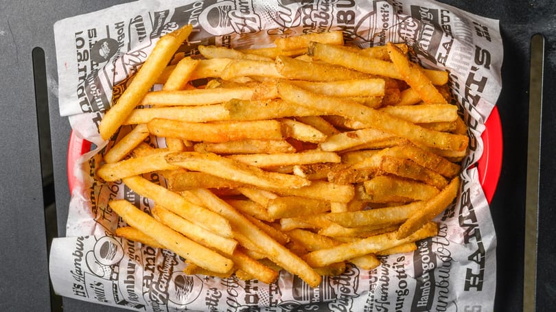 A red basket filled with golden-brown french fries, seasoned and served on branded paper.